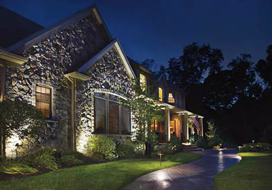 Elegant home with stone facade illuminated by outdoor pathway lighting, showcasing a beautifully lit landscape at night – ideal for enhancing curb appeal and security.