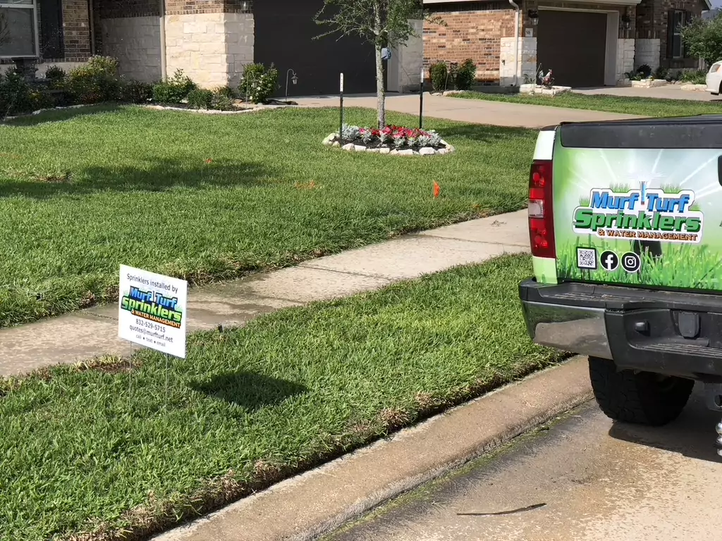 Truck with Murf Turf Sprinklers & Water Management branding parked next to a yard with a sign indicating sprinkler installation.