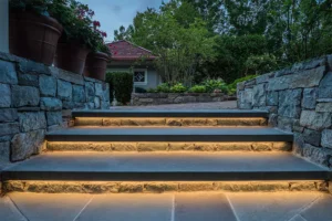Stylish outdoor steps with integrated lighting, highlighting stone textures and providing safe, illuminated access to a beautifully landscaped yard in the evening.