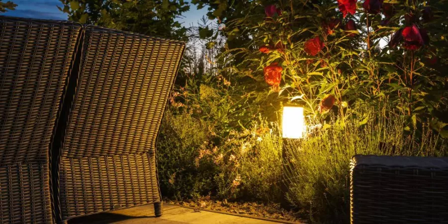 Outdoor patio with wicker furniture and soft garden lighting illuminating plants and flowers.